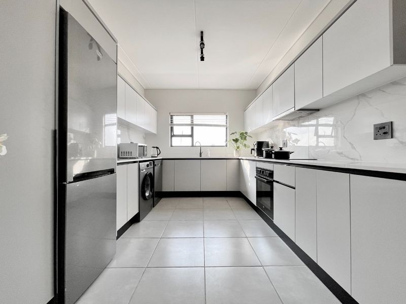 Modern galley-style kitchen featuring sleek white cabinetry, marble-look splashbacks, integrated oven, extractor fan, and neutral tiled flooring.