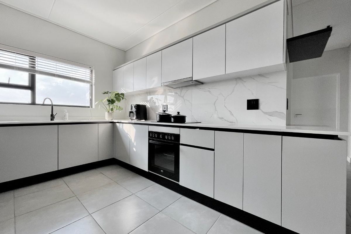 Modern kitchen featuring sleek white cabinetry, marble-look splashback, integrated oven and hob, and tiled flooring.