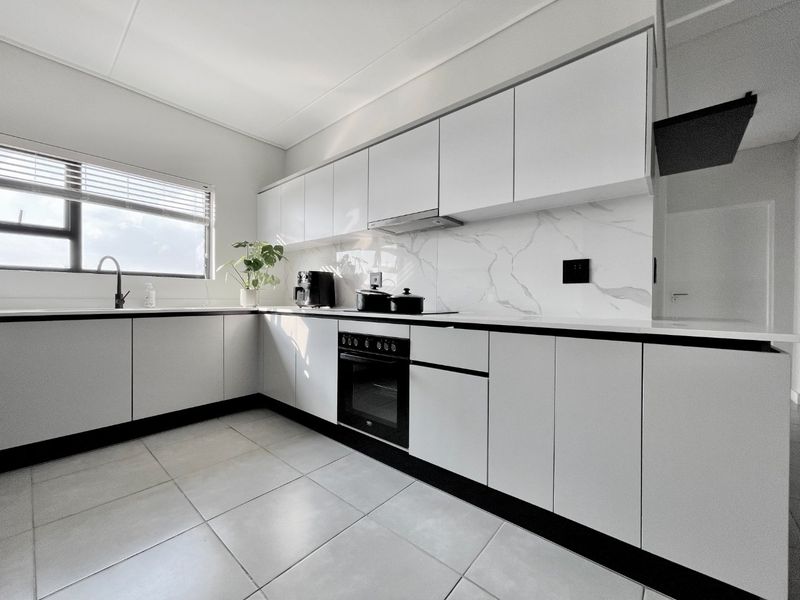 Modern kitchen featuring sleek white cabinetry, marble-look splashback, integrated oven and hob, and tiled flooring.
