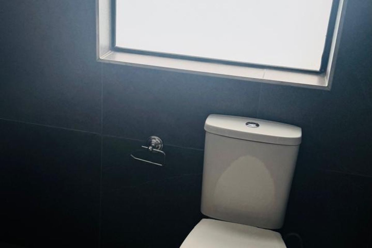 A clean, modern bathroom featuring dark floor-to-ceiling wall tiles, a white toilet, and a top-hung window providing natural light.