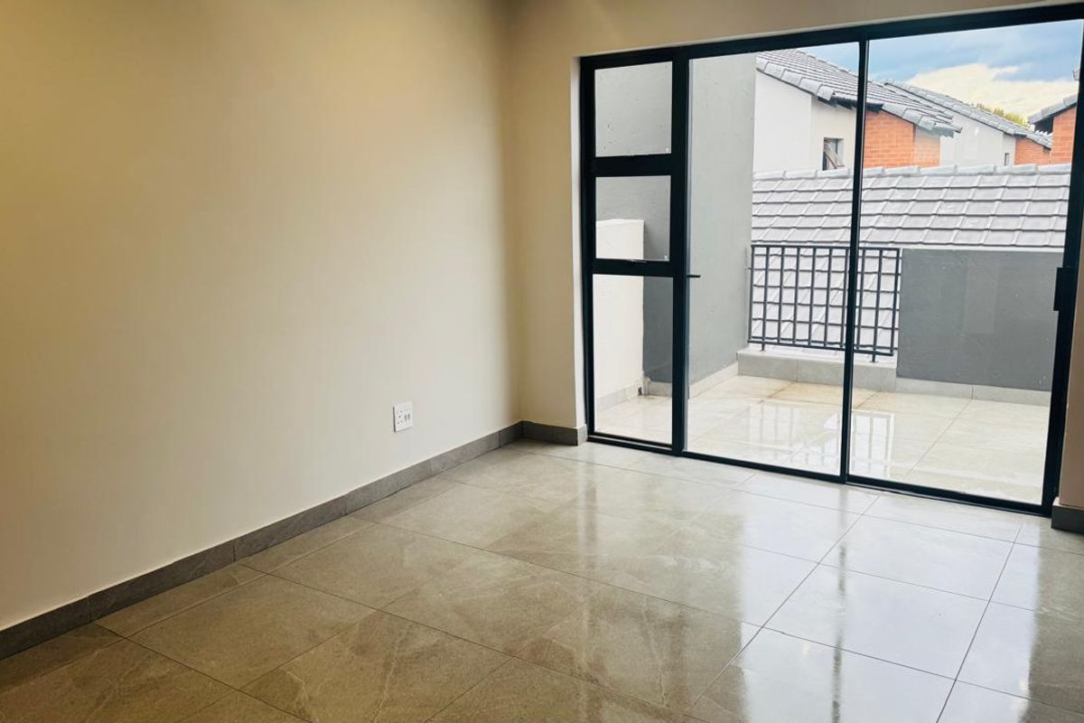 A bright, empty bedroom featuring modern tiled flooring and a large sliding glass door that opens onto a private balcony.
