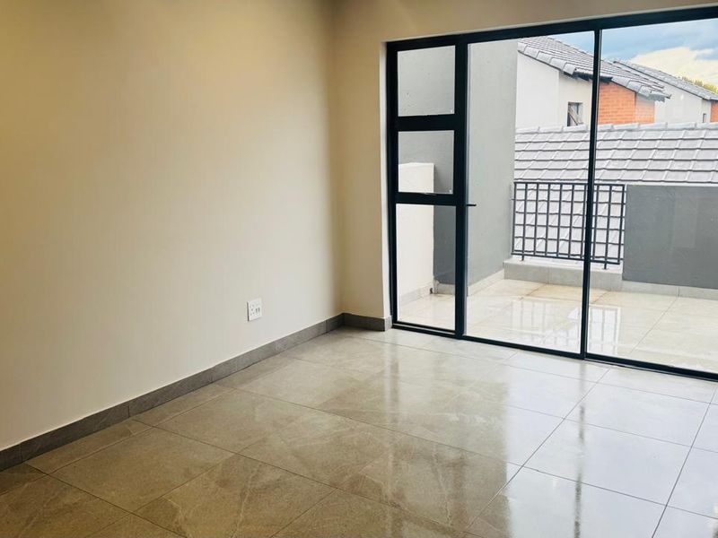A bright, empty bedroom featuring modern tiled flooring and a large sliding glass door that opens onto a private balcony.