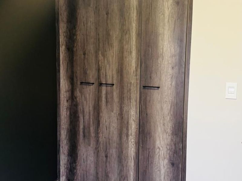 A clean, modern bedroom space featuring a large, wood-grain finish built-in wardrobe and neutral tiled flooring.