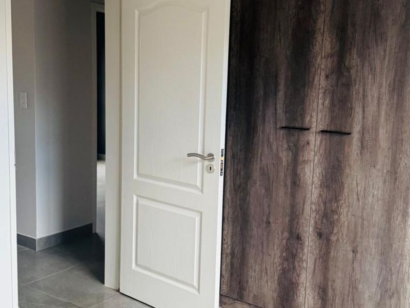A clean, modern bedroom featuring neutral tiled flooring and dark wood-finish built-in cupboards, offering a bright and functional living space.