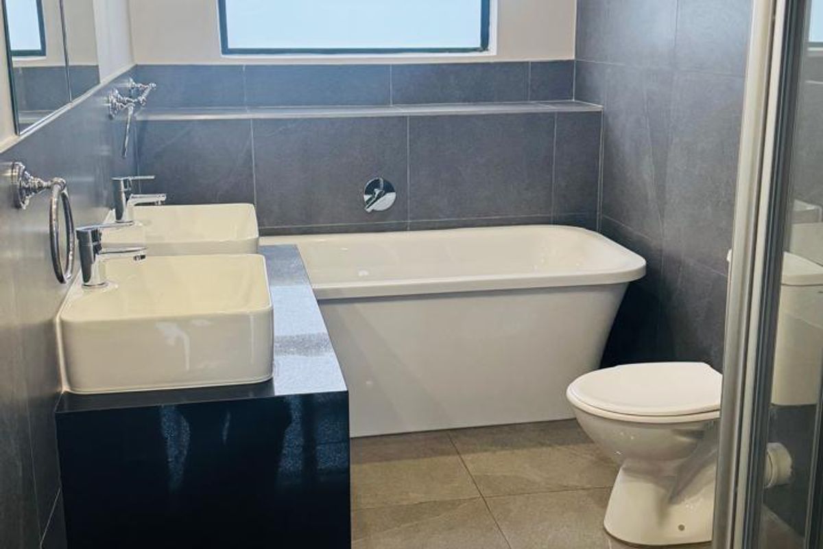 Modern bathroom featuring a double vanity, freestanding bathtub, separate shower enclosure, and contemporary grey wall and floor tiling.