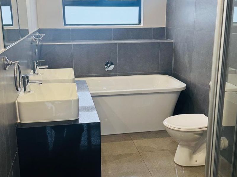 Modern bathroom featuring a double vanity, freestanding bathtub, separate shower enclosure, and contemporary grey wall and floor tiling.