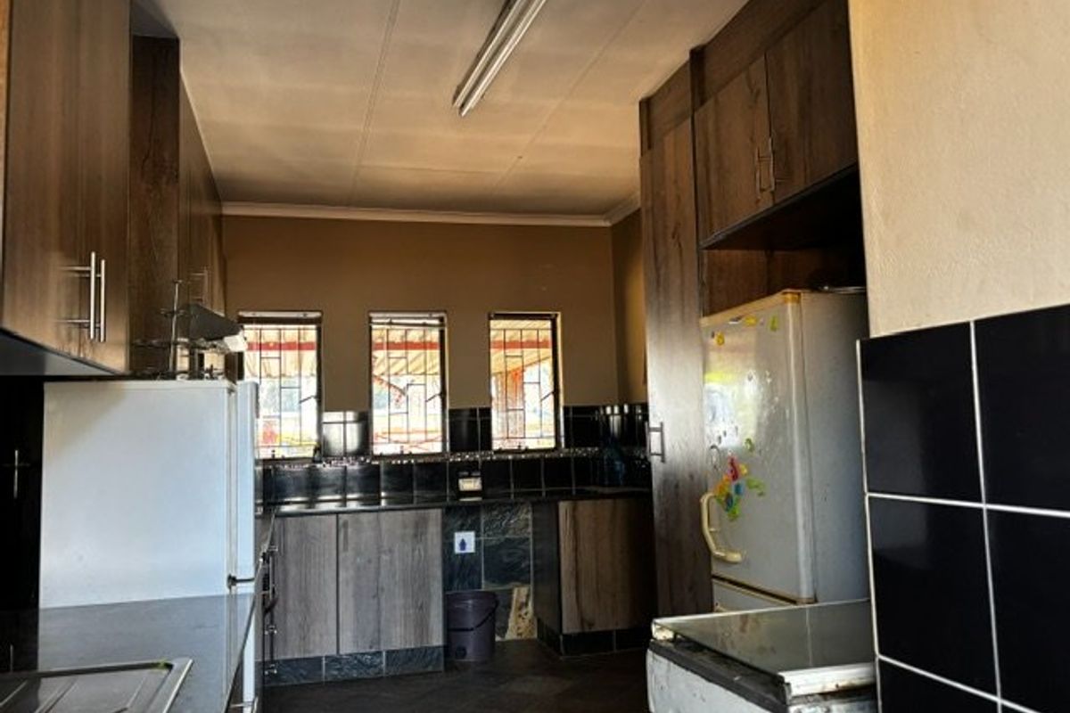 A functional kitchen featuring dark laminate cabinetry, stone countertops, and tiled backsplash, with security bars on the windows and standard fluorescent lighting.