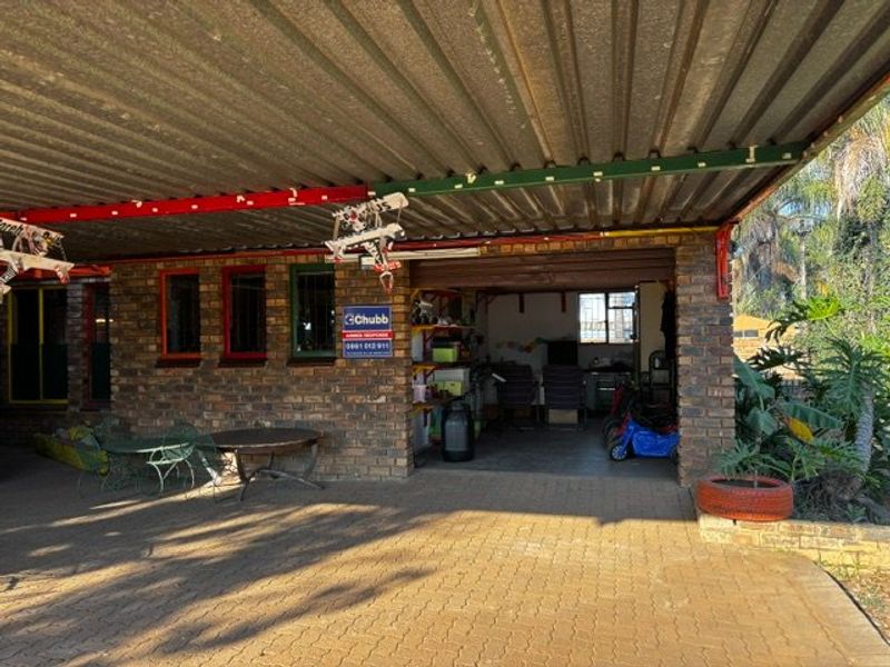 A functional facebrick garage with a corrugated metal roof and paved driveway, featuring integrated security signage.