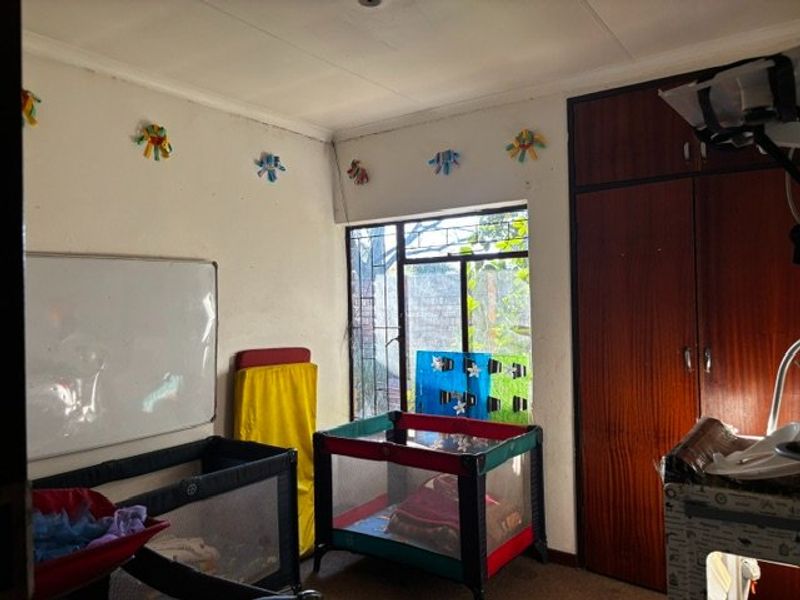 A bedroom featuring built-in wooden cupboards and a window with security bars, offering a functional space with potential for cosmetic updates.