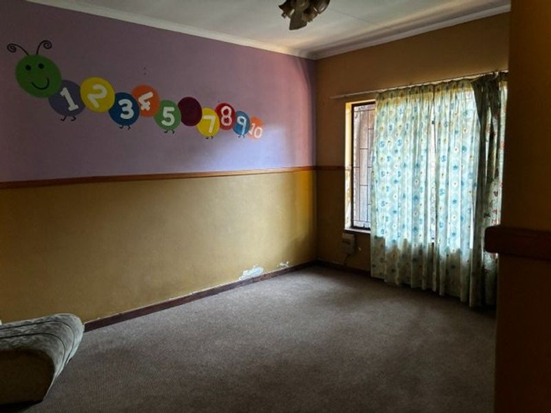 A spacious bedroom featuring carpeted flooring, a window with security bars, and decorative wall finishes, offering a blank canvas for renovation.