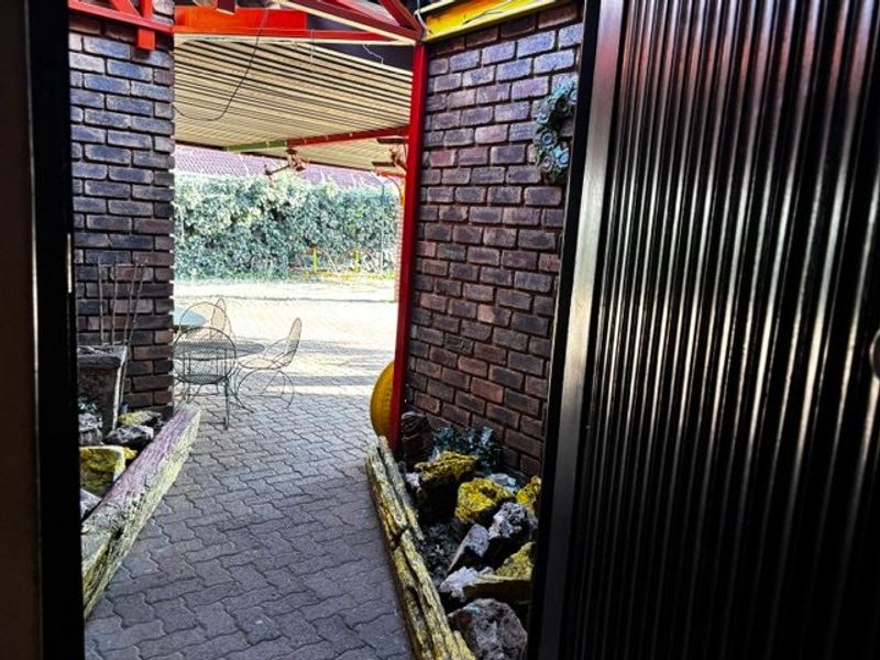 A covered outdoor patio area featuring brick walls, paved flooring, and built-in planter boxes, providing a sheltered space for outdoor relaxation.