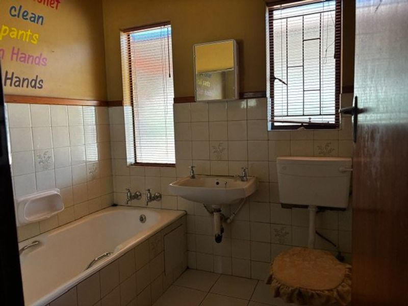 A dated bathroom featuring a standard bathtub, wall-mounted basin, and toilet, with tiled finishes and security bars on the windows.