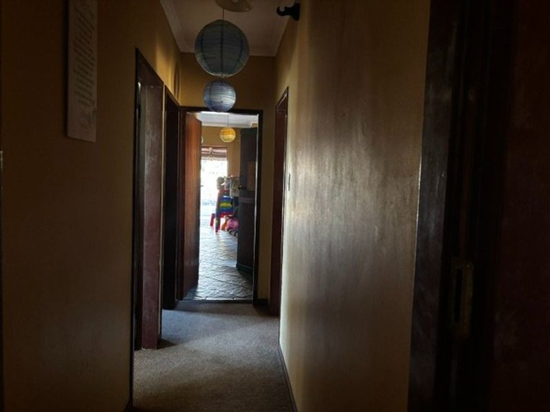 A narrow residential hallway with carpet flooring and dark wall paint, leading towards an open doorway with natural light.