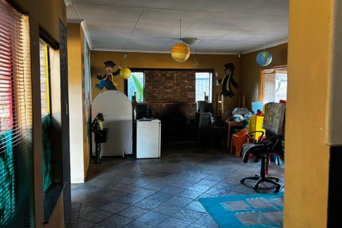 A living area featuring tiled flooring and a brick fireplace, currently used as a play area with dated wall finishes.