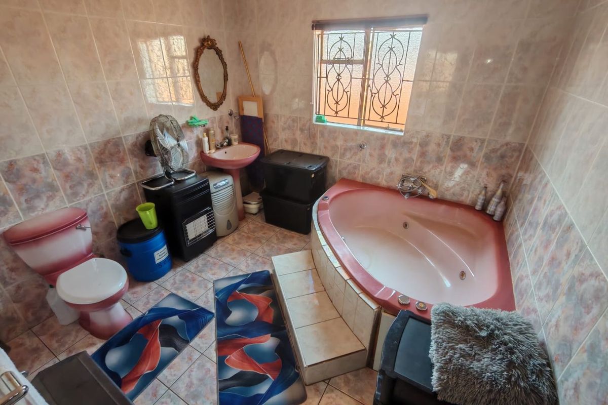 A dated bathroom featuring a corner bathtub, pedestal basin, and toilet with full-height wall tiling and security bars on the window.