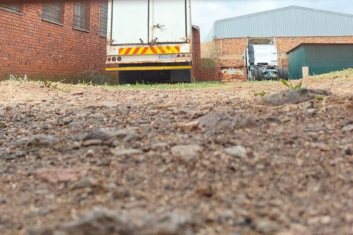 A view of the rear vacant land area featuring a gravel surface and adjacent brick boundary wall.
