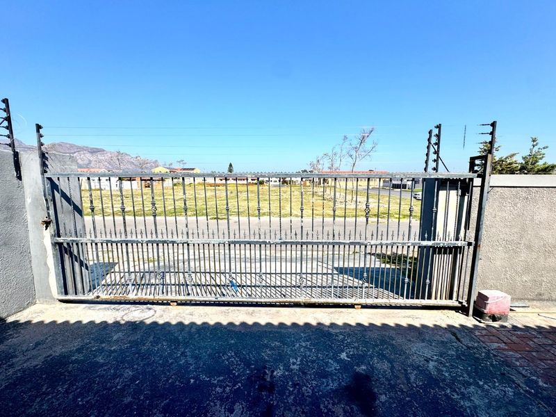 Front view of the property entrance featuring a metal sliding gate, electric fencing, and a concrete driveway.