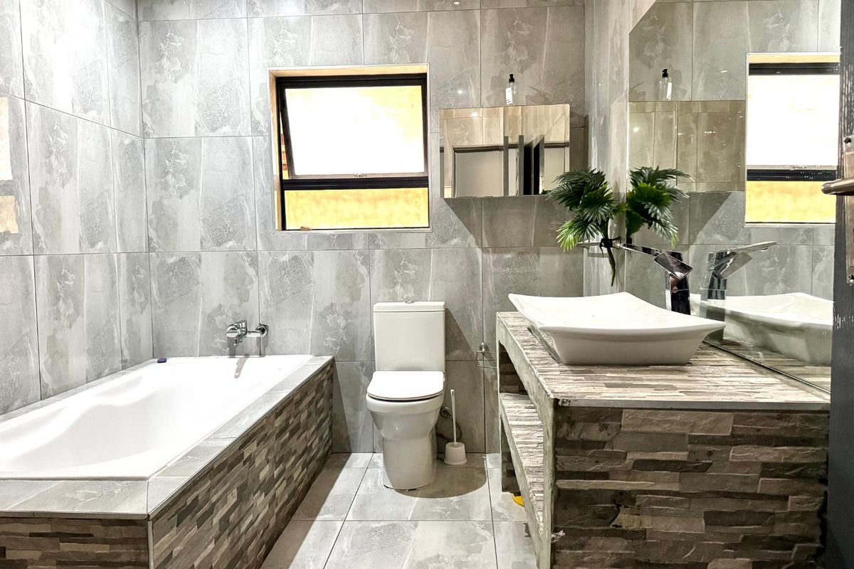 Modern bathroom featuring full-height grey tiling, a built-in bathtub, a stone-clad vanity with a vessel sink, and a wall-mounted mirror.
