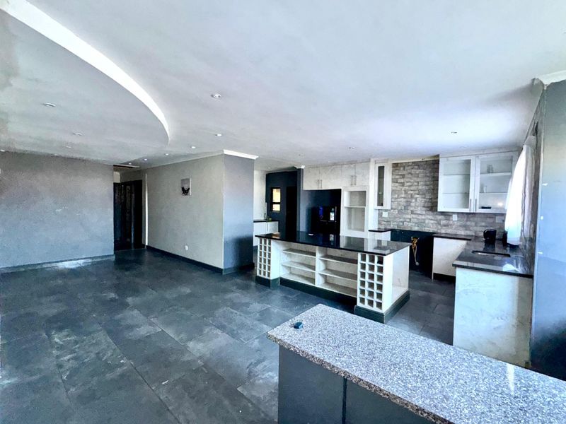 Spacious open-plan kitchen and living area featuring a central island, granite countertops, and a stone feature wall, awaiting final finishing touches.
