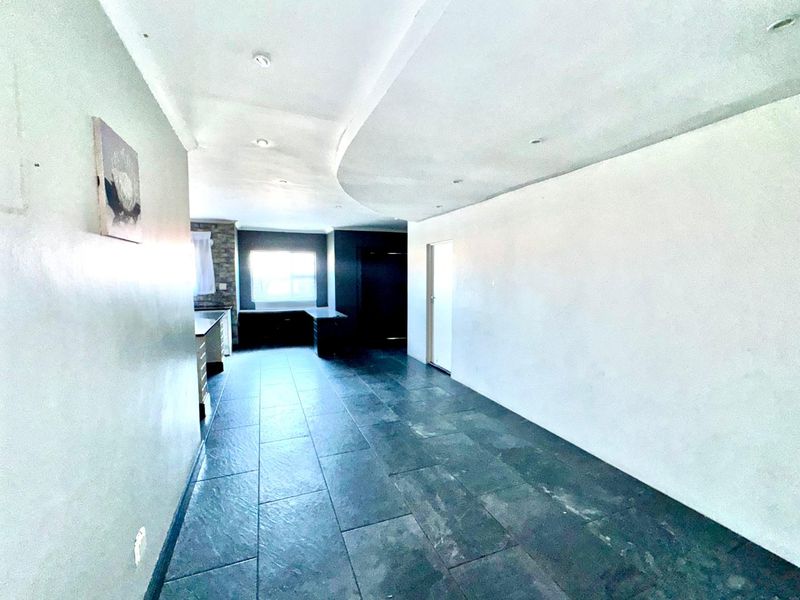 An open-plan living area featuring dark tiled flooring, a distinctive curved bulkhead ceiling with recessed lighting, and a neutral wall palette.