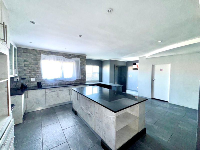 Spacious modern kitchen featuring a central island, stone countertops, stone veneer feature wall, and dark tile flooring with recessed lighting throughout.