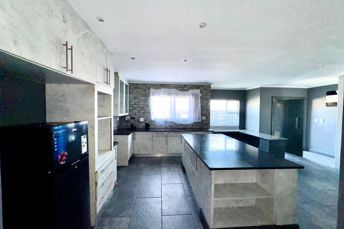 Modern kitchen featuring a large central island with stone countertops, extensive built-in cabinetry, and stylish tiled flooring with recessed lighting.