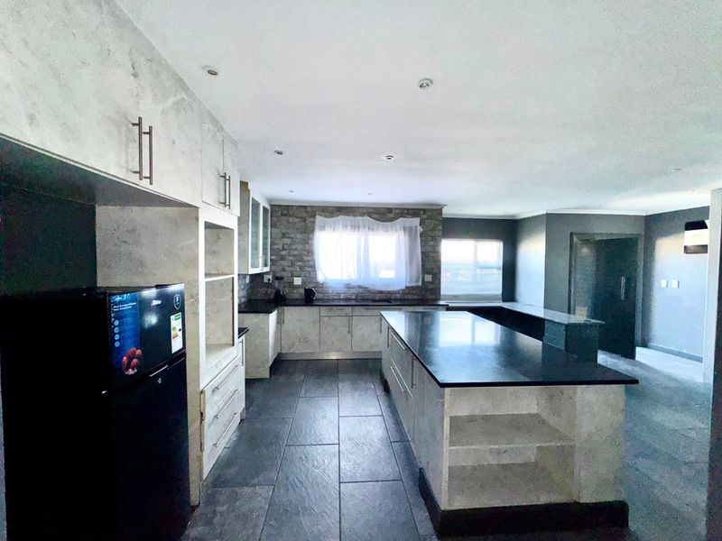 Modern kitchen featuring a large central island with stone countertops, extensive built-in cabinetry, and stylish tiled flooring with recessed lighting.