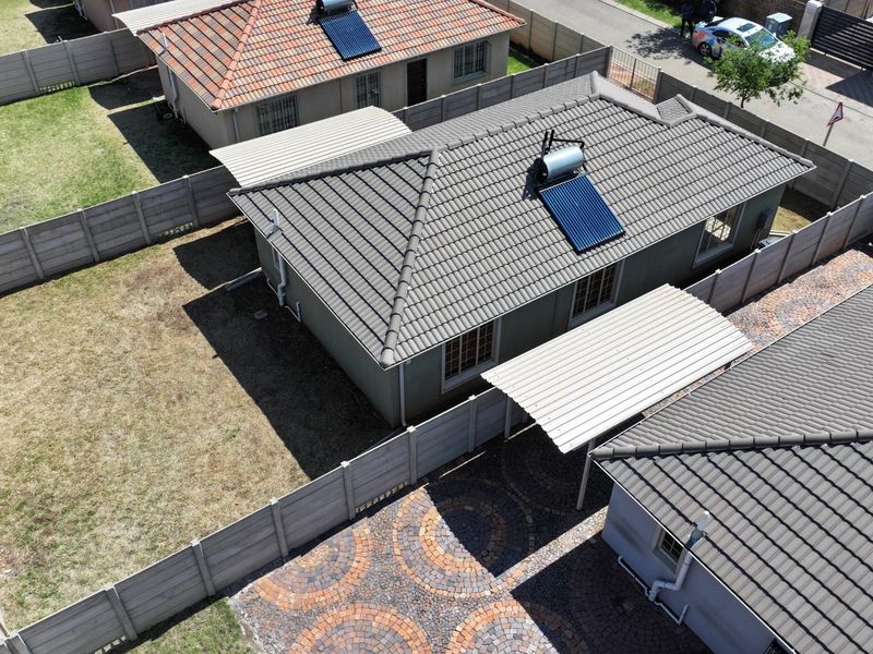 Aerial view of the property featuring a tiled roof with solar water heating, a paved driveway, carport, and enclosed garden area.