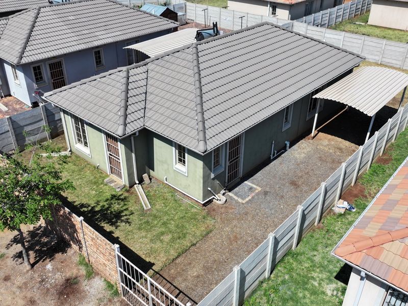 Aerial view of a residential property featuring a tiled roof, a carport, and a fenced yard with a gravel driveway area.