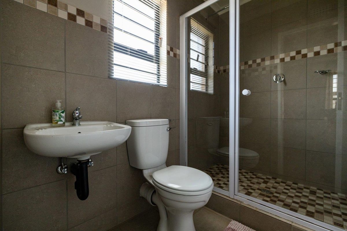A functional bathroom featuring a wall-mounted basin, a standard toilet, and a glass-enclosed shower with neutral tiled finishes.