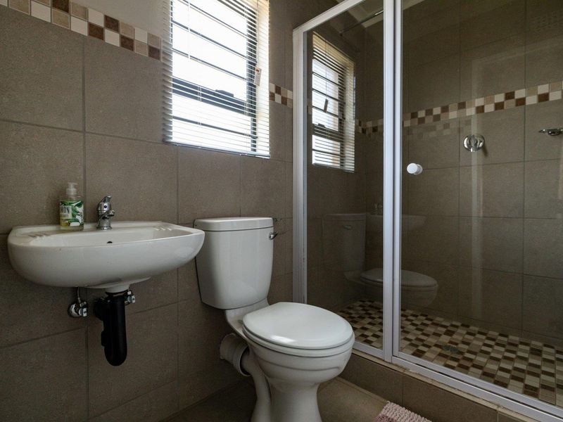 A functional bathroom featuring a wall-mounted basin, a standard toilet, and a glass-enclosed shower with neutral tiled finishes.