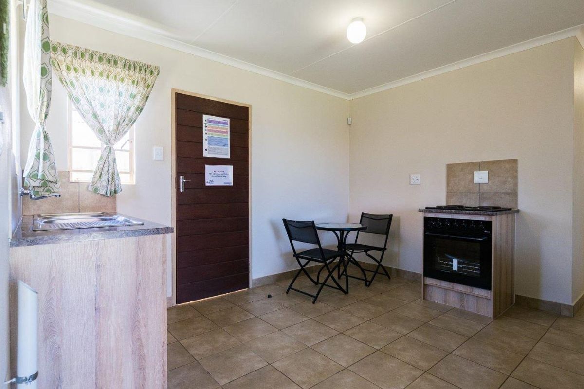 Compact kitchen area featuring tiled flooring, built-in cabinetry, a stainless steel sink, and a freestanding oven with a tiled splashback.