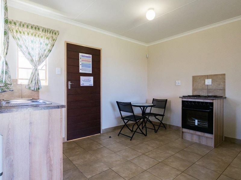 Compact kitchen area featuring tiled flooring, built-in cabinetry, a stainless steel sink, and a freestanding oven with a tiled splashback.