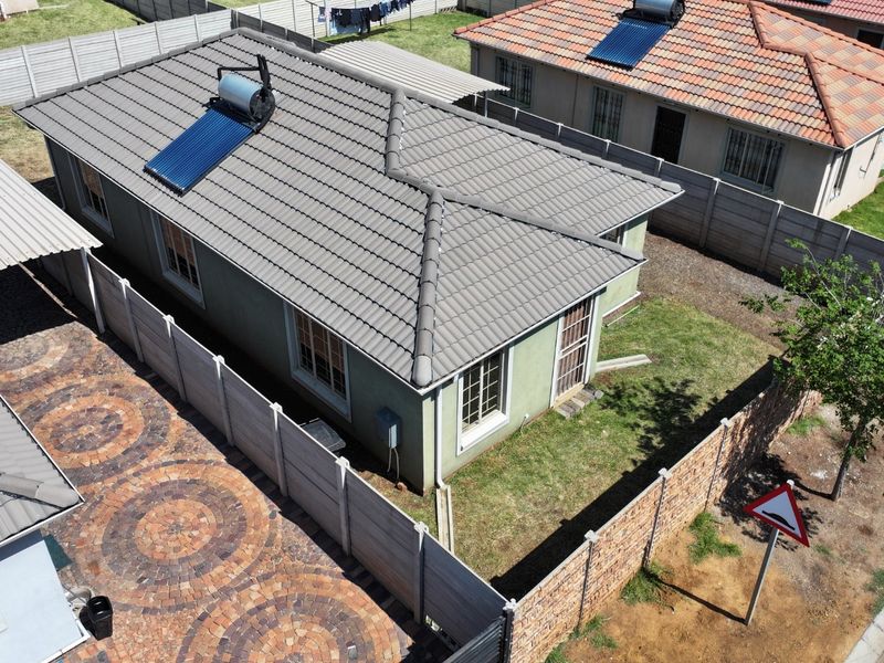 Aerial view of a residential property featuring a tiled roof with a solar water heater, paved driveway, carport, and enclosed garden area.