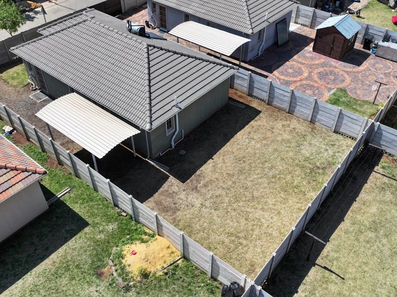 Aerial view of a residential property featuring a tiled roof house, a carport, and a fenced backyard with a paved area.