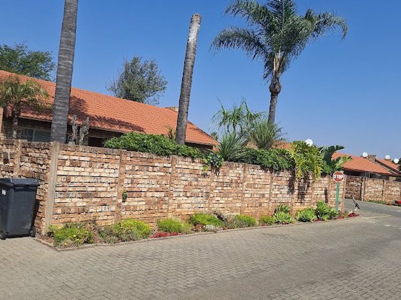 A view of the townhouse exterior featuring a brick boundary wall, paved driveway, and tiled roof structure.