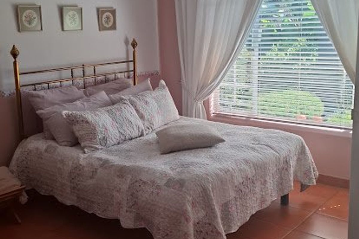 A bedroom featuring terracotta floor tiles, a large window with venetian blinds, and neutral wall finishes.