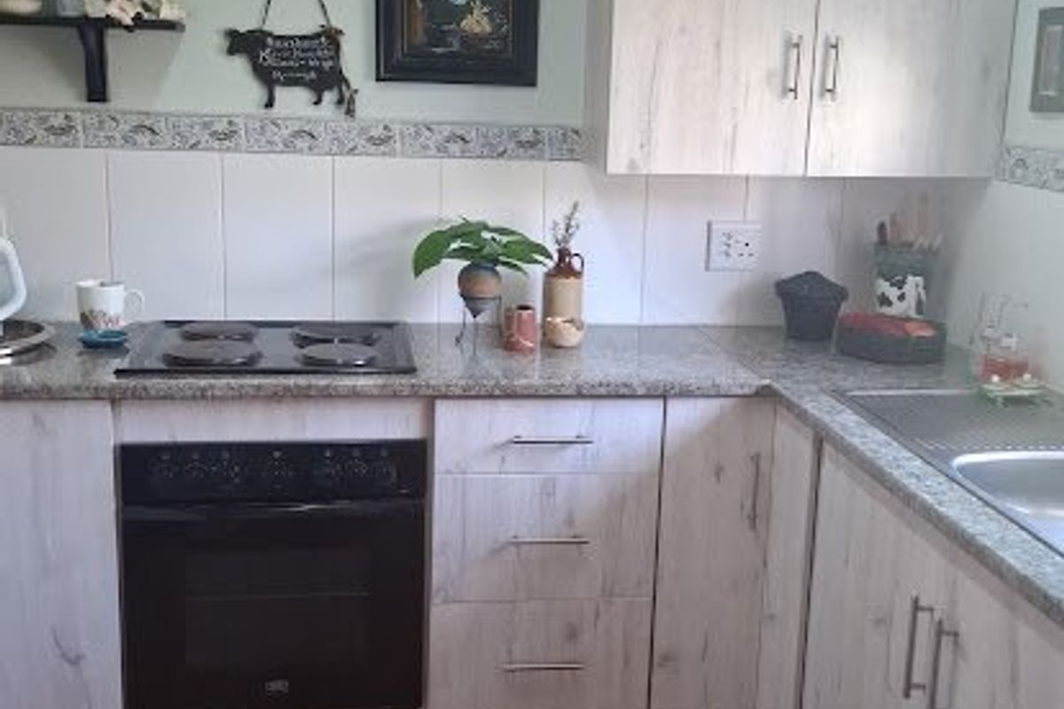 A functional kitchen featuring light wood-grain cabinetry, granite countertops, a built-in oven with electric hob, and durable ceramic floor tiles.