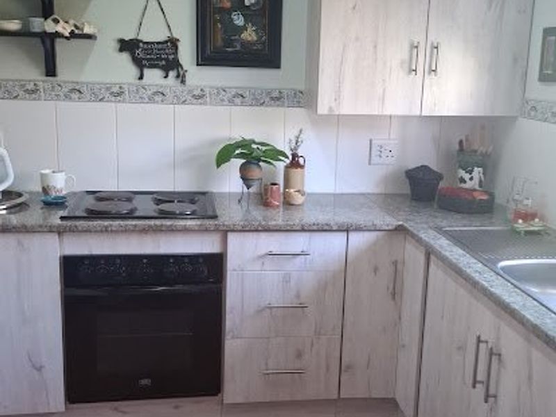 A functional kitchen featuring light wood-grain cabinetry, granite countertops, a built-in oven with electric hob, and durable ceramic floor tiles.