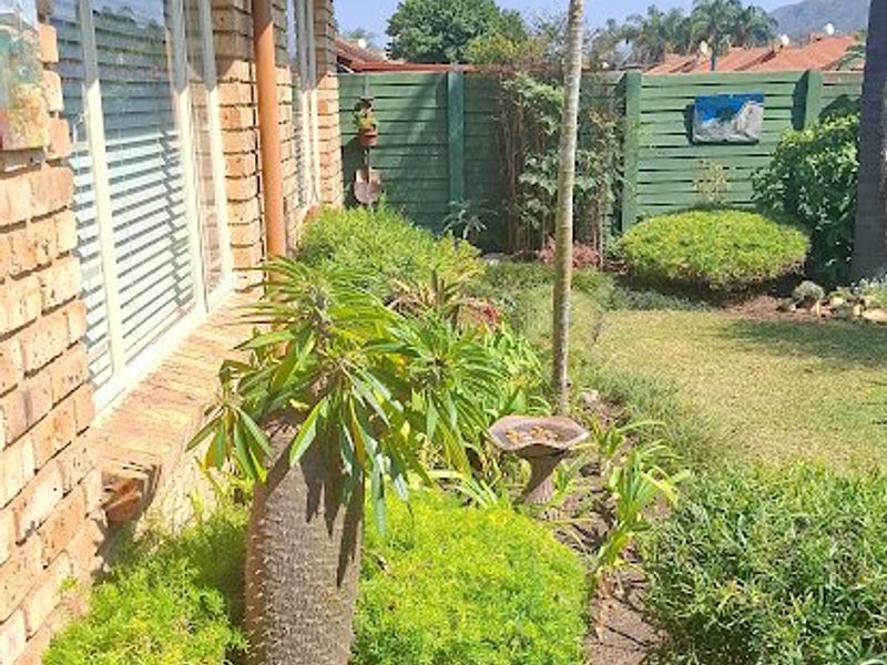 A well-maintained rear garden area featuring a brick townhouse facade, paved walkway, and established landscaping with a timber boundary fence.