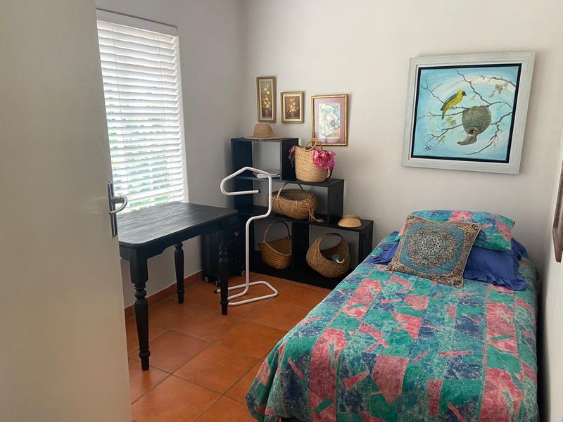 A compact bedroom featuring terracotta floor tiles and venetian blinds, offering a functional space with neutral wall finishes.