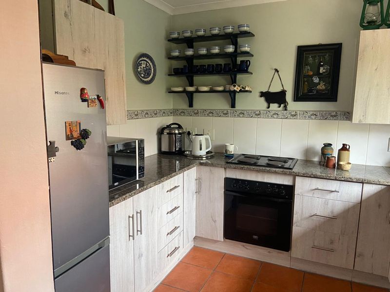 A functional kitchen featuring light wood-grain cabinetry, granite countertops, a built-in oven with electric hob, and durable ceramic floor tiles.