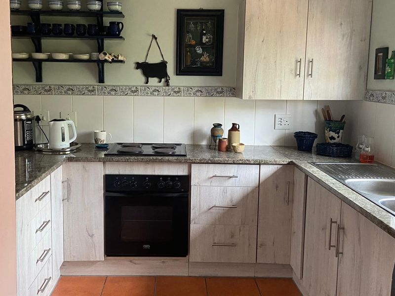 A functional kitchen featuring light wood-grain cabinetry, granite countertops, a built-in electric oven and hob, and durable terracotta floor tiles.