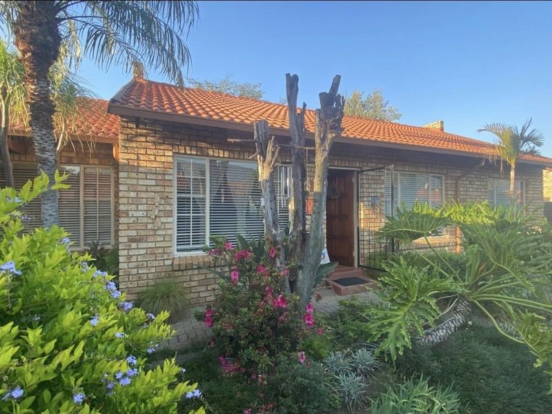 Front elevation of a face brick townhouse featuring a terracotta tiled roof, secure entrance with a timber door, and established garden landscaping.