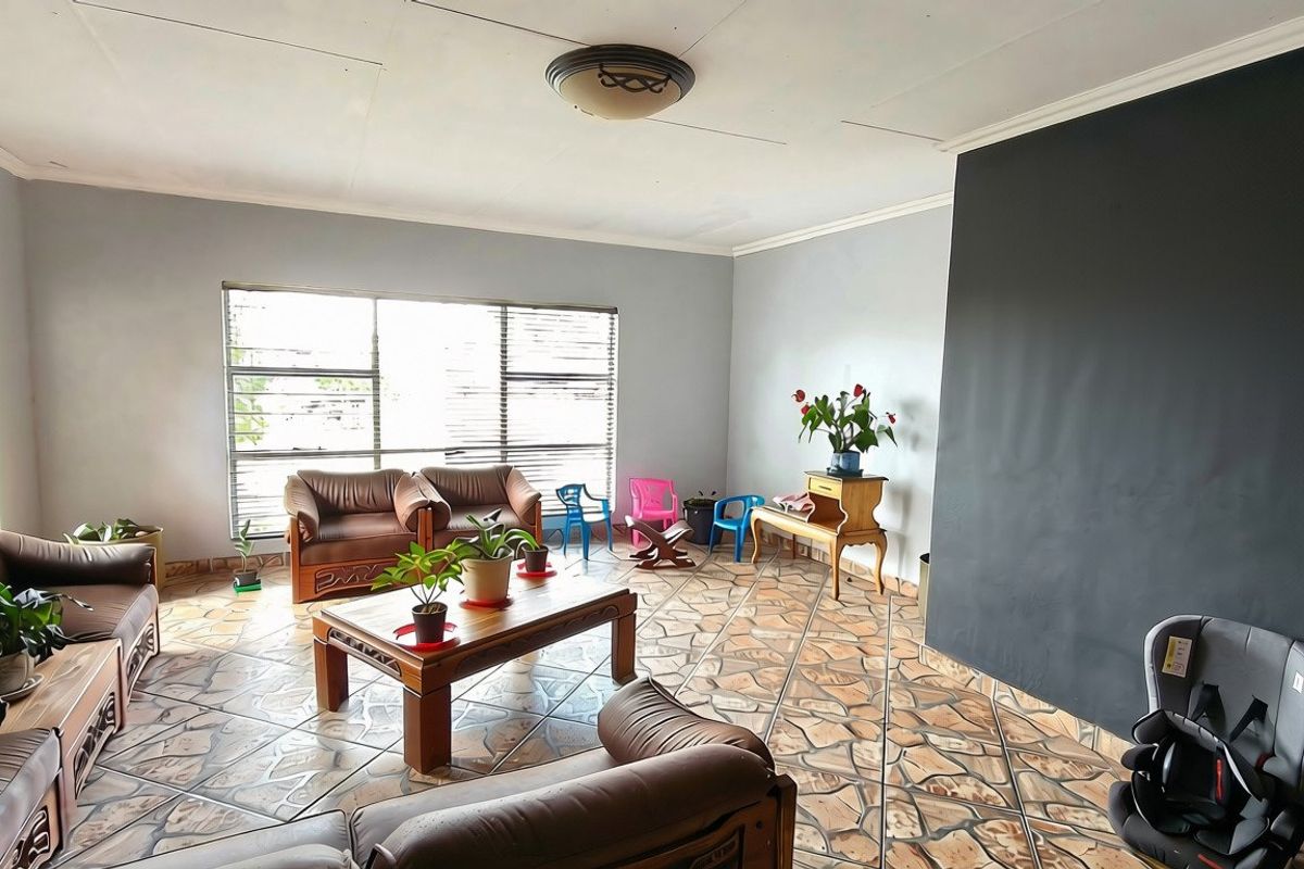 Spacious living room featuring unique stone-patterned tiled flooring, large windows with venetian blinds, and a prominent dark accent wall.