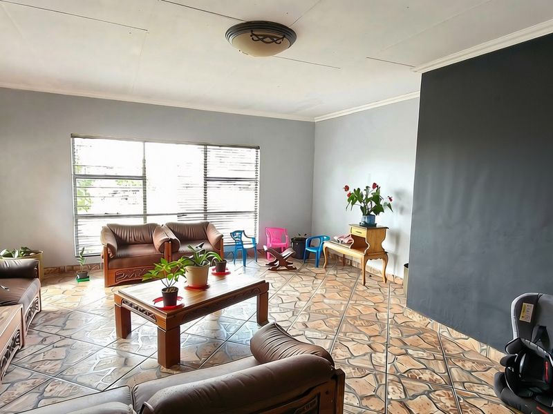 Spacious living room featuring unique stone-patterned tiled flooring, large windows with venetian blinds, and a prominent dark accent wall.