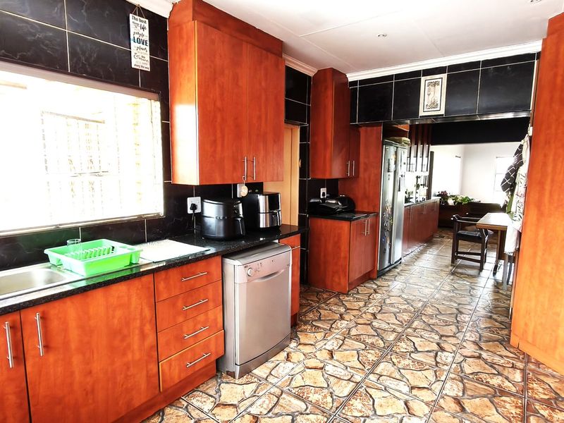 Spacious kitchen featuring warm wooden cabinetry, granite countertops, a double basin sink, and distinctive tiled flooring, offering a functional layout for family living.