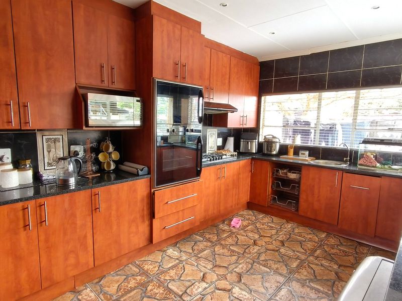 A functional kitchen featuring warm-toned wooden cabinetry, granite countertops, a built-in oven, hob, and a tiled backsplash with natural light.