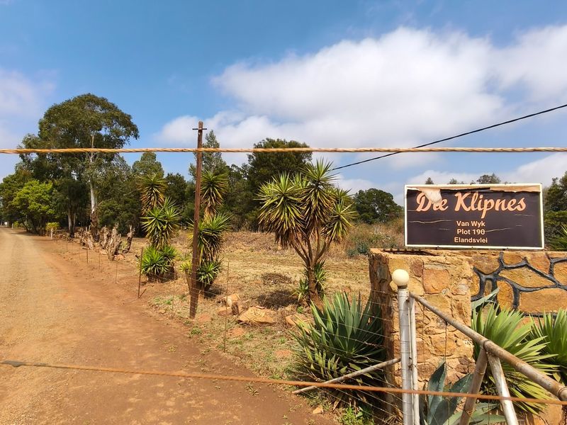 Entrance to the farm property featuring a stone masonry pillar, property signage, and a gravel driveway leading into the rural landscape.