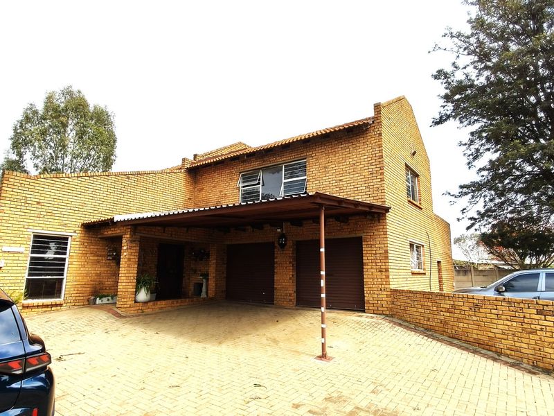 Front elevation of a double-story face brick farmhouse featuring a paved driveway, double garage, and an attached carport.